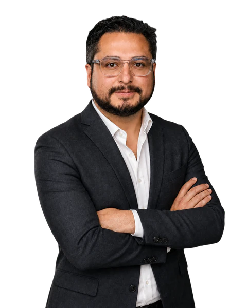 Edwin Mata wearing glasses, a dark suit and white shirt, with arms crossed